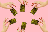 Fototapeta  - Frame of female hands with crispy seaweed on the pink background with copy space. Dry nori sheets korean or japanese texture. Flat lay. Healthy food concept.
