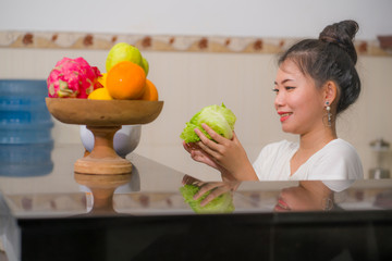 vegetable food and diet - home lifestyle portrait of young beautiful and happy Asian Chinese woman at domestic kitchen smiling cheerful in healthy nutrition and dieting concept