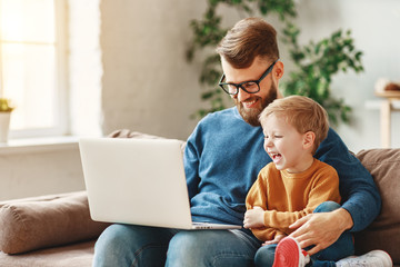 Happy father and son using laptop on sofa.