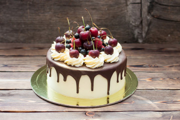 Wall Mural - Homemade cake with melted chocolate decorated with whipped cream and fresh cheries on top. Rustic wooden background.