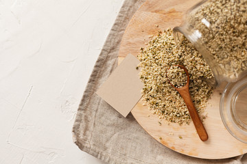 Cannabis kernels in a glass jar on a white table with a wooden spoon