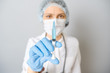 © Iurii - Portrait of young woman in medical uniform, protective mask and cap with medical syringe in hand. Isolated on gray background
