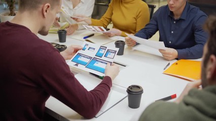 Wall Mural - Female marketing manager giving printouts with application interface templates for different devices to colleagues while sharing ideas in team meeting