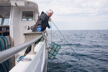 Man Lowering Lobster Cage Into The Water