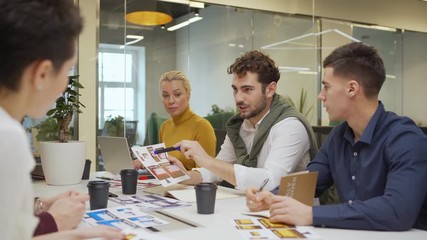 Wall Mural - Tracking shot of chief designer presenting printout with website interface templates for different devices to colleagues while sharing ideas in team meeting
