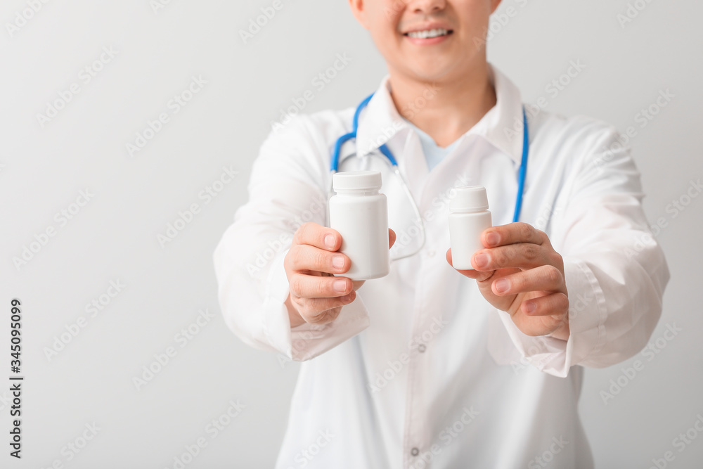 Male doctor with pills on light background