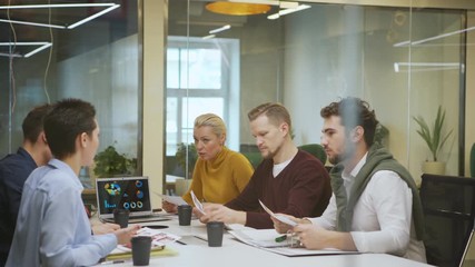 Wall Mural - Through glass wall tracking shot of business team planning work sitting at table during meeting in boardroom