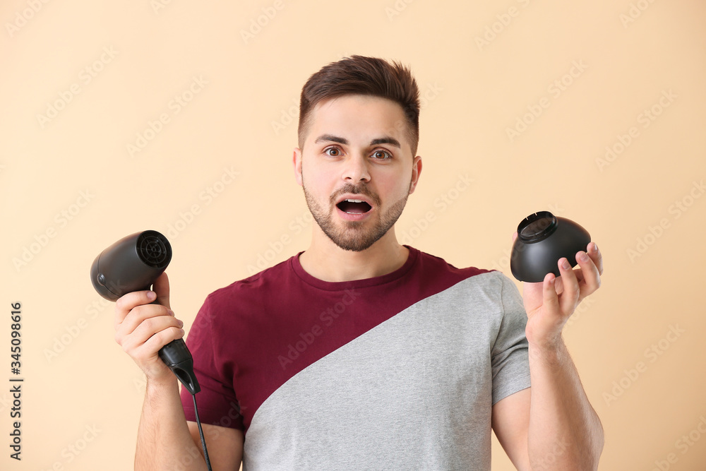 Shocked young man with hair dryer on color background
