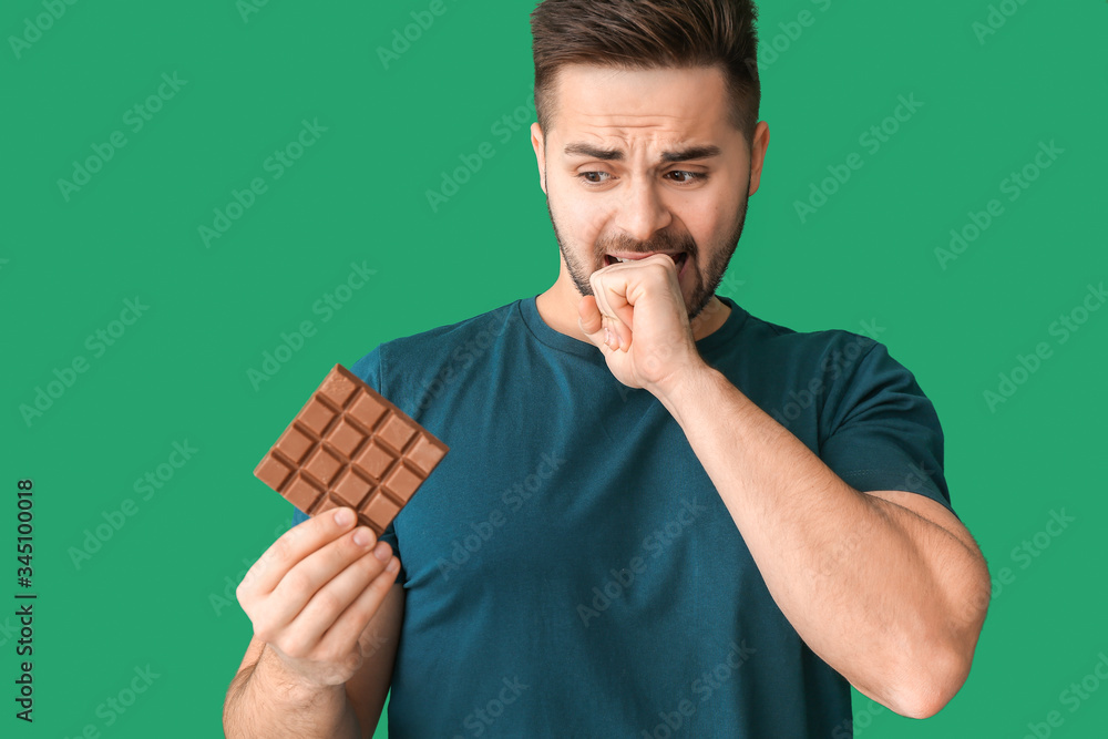 Bothered young man with tasty chocolate on color background