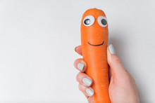 Hand Holding Carrot With Fun Googly Eyes And Smile On White Background. Diet Concept