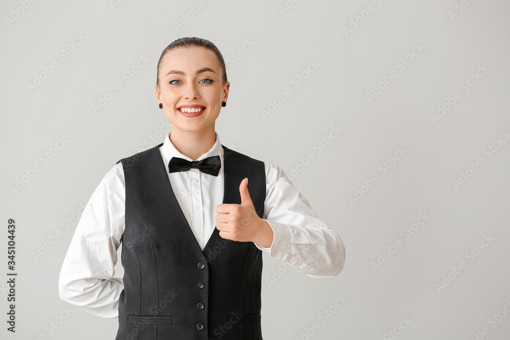 Beautiful female waiter showing thumb-up on grey background