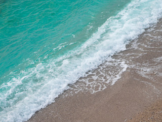 Aerial view of turquoise sea wave reaching the coastline. The picture is divided diagonally by the surf strip on the sea and sand.