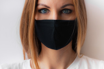 Close-up portrait of a young woman in a black medical mask and blue eyes and white T-shirt on white background. Quarantine, coronavirus epidemic pandemic, covid-19. Stay home concept. Virus protection