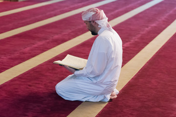 Poster - Young Arabic Muslim man reading Koran and praying. Religious muslim man reading holy koran inside the mosque.