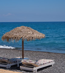 Wall Mural - Relaxing holiday landscape in Santorini with straw umbrella and sunbeds with thick mattresses on the beach by the sea 