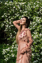 beautiful girl in a dress in the sunlight with closed eyes enjoys the warmth against the background of white flowers in a flowering garden