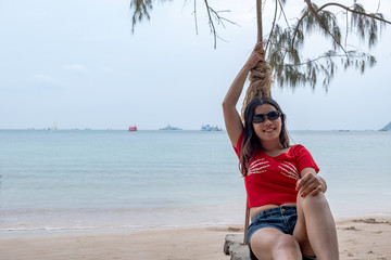 Wall Mural - Smiling thai lady on a swing on the tropical beach in sunny day. Asian girl enjoy at the beach.