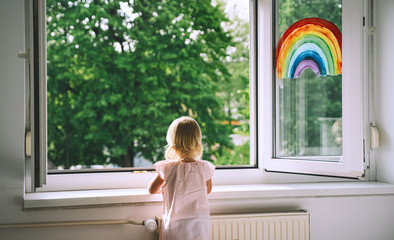 Little girl looks out  open window at home at spring time.