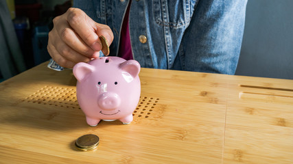 A hand is putting the coins in a pink piggy bank isolate in wooden background.