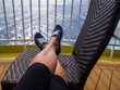 Woman's legs and tennis shoes shown resting on chair on the back deck of a cruise ship.