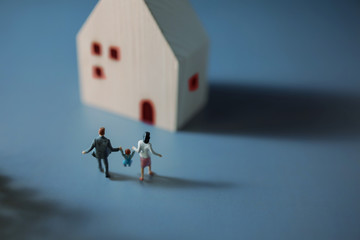 Happy Family Concept. Miniature Figure of Father, Mother and Son Holding Hands and Walking into the House