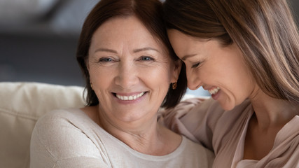 Wall Mural - Close up smiling mature mother and daughter hugging, touching heads, expressing love and care, young woman and middle aged mum enjoying tender moment, two generations good relationship