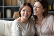 © fizkes - Happy mature mother and adult daughter hugging close up, having fun, sitting on couch at home, smiling woman embracing older mum, spending leisure time together, two generations good relationship
