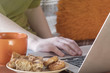 © Николай Батаев - A girl whose face is not visible is sitting at a laptop with a cup of hot drink and cookies. Cozy pastime.
