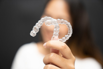 Women hand hold inivisalign braces, transparent aligner, invisible retainer or orthodontic silicone trainer with blur mile in background. A way to have a beautiful smile.