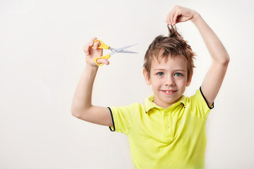 The boy cuts his own overgrown hair, there is no way to go to the hairdresser, because quarantine, self-isolation. Concept home quarantine. A boy dressed in a bright T-shirt, holding scissors