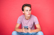 © mimagephotos - Close up young man sitting by red wall with mobile phone