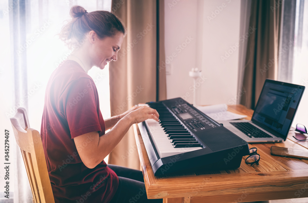 Young girl woman learns to sing and play the piano from a video conference from a laptop. Education video calls self education - obrazy, fototapety, plakaty 