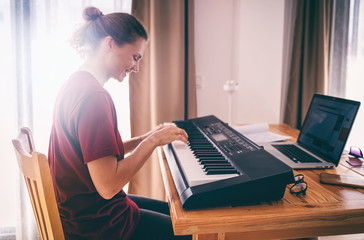 young girl woman learns to sing and play the piano from a video conference from a laptop. education 