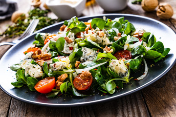 Fresh salad - blue cheese, cherry tomatoes, vegetables and walnuts on wooden background
