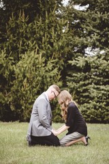 Poster - A couple praying together on their knees on a grassy lawn with trees in the background