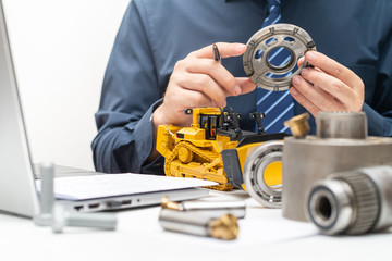 Professional mechanic engineer inspecting valve plate of hydraulic piston pump and writing reports for during working day in office, repair maintenance heavy machinery concept