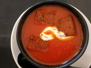 hot cream tomato soup with croutons in a black bowl on the table, top view.