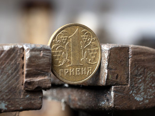 Wall Mural - hryvnya coin clamped in a metal vise. Currency and Ukrainian economy under the onslaught, the concept of financial problems and crisis