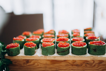 Rolls pieces with red caviar. Green rolls on the buffet table.