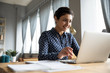 © fizkes - Head shot smiling pretty indian girl sitting at table, looking at laptop screen. Happy hindu ethnic woman reading message email with good news, chatting with clients online, working remotely.