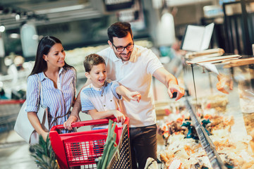 Happy family with child and shopping cart buying food at grocery store or supermarket