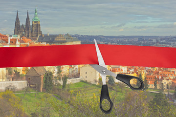 Wall Mural - End of quarantine covid-19. The beginning of travel, the opening of borders. Scissors cut a red ribbon with a view of Prague, Czech Republic