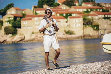 Outdoor fashion portrait of handsome stylish tourist man posing at the beach.