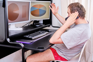 A man in red shorts is sitting at home at the computer and talking on the phone. The concept of remote work during the quarantine period due to the flu epidemic.