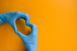Two hands in blue medical gloves folded in the shape of a heart on an orange background