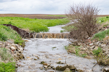 Water flowing in farm field waterway after heavy rain and storms caused flooding. Concept of soil erosion, water runoff control and management