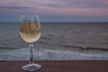 Glass of white wine in the sunset overlooking the sea. Glass of wine on the wooden jetty at sunny sea.