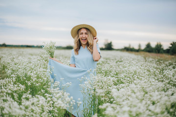 beautiful blonde girl in a field of daisies. woman in a blue dress in a field of white flowers. girl with a bouquet of daisies. summer tender photo in the village. wildflowers. girl in a straw hat