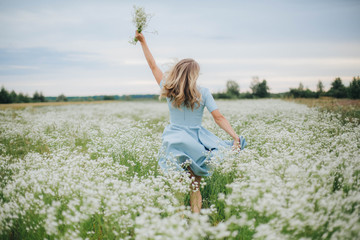 beautiful blonde girl in a field of daisies. wreath of wildflowers on his head. woman in a blue dress in a field of white flowers. charming girl with a bouquet of daisies. summer tender photo