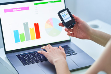 Diabetic patient using remote sensor and computer for control and monitoring glucose blood levels graphs. Medical technology in diabetes treatment, healthcare